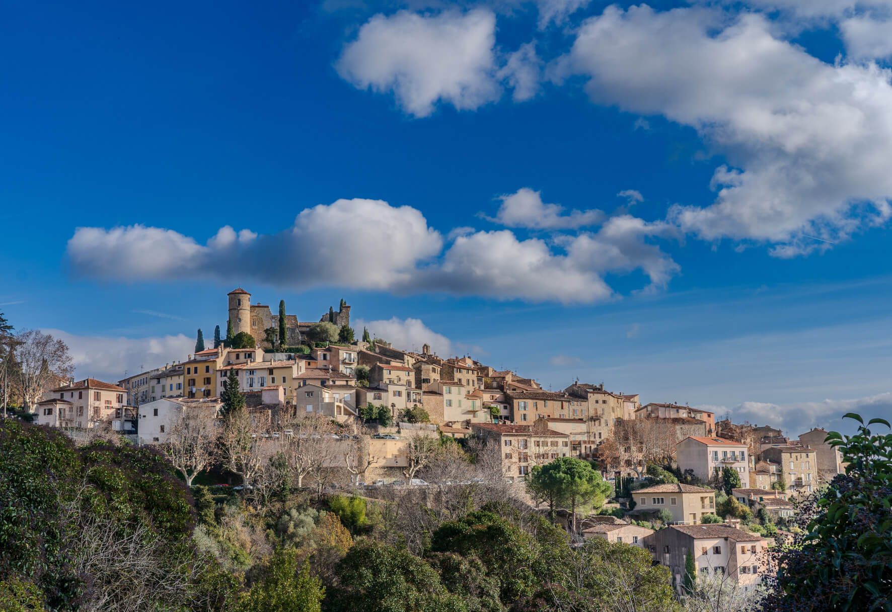 Eine malerische Stadt mit einem alten Schloss, umgeben von sanften Hügeln und strahlend blauem Himmel.