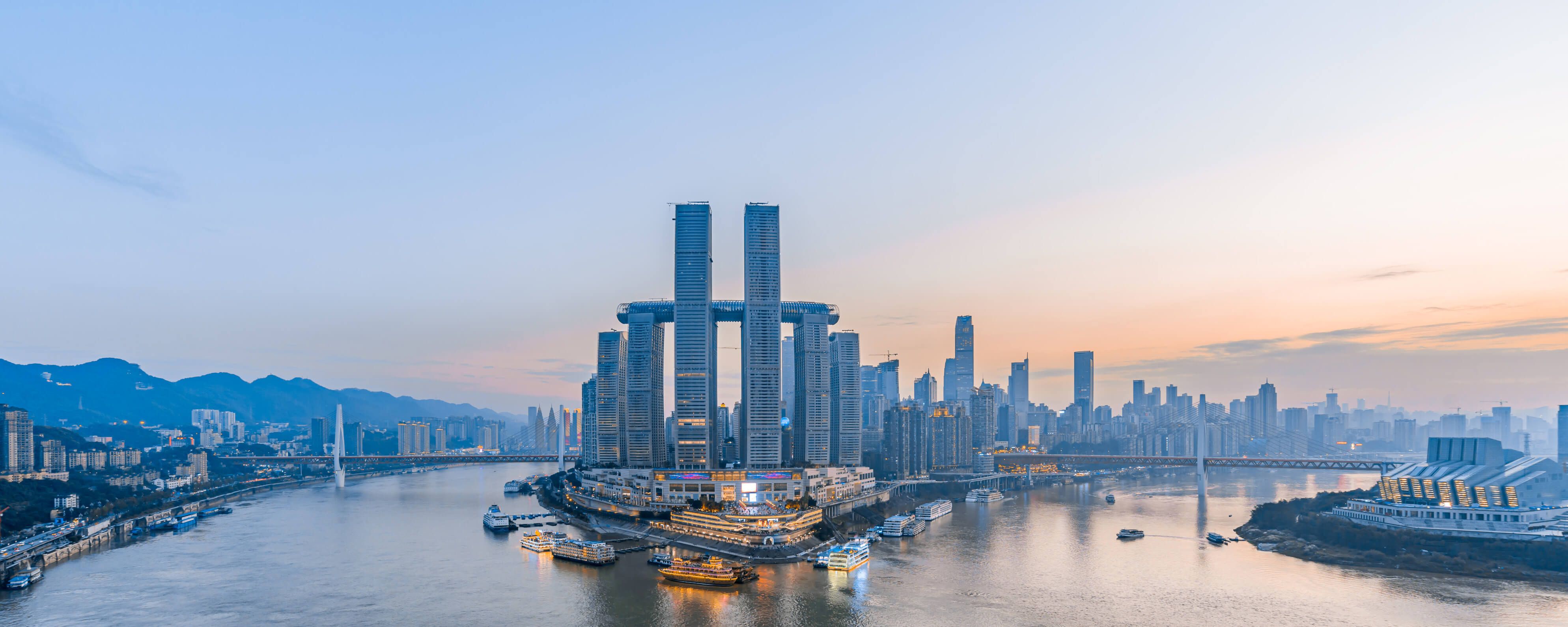 Eine beeindruckende Skyline über einem Fluss, umgeben von Bergen und modernen Gebäuden bei Sonnenuntergang.