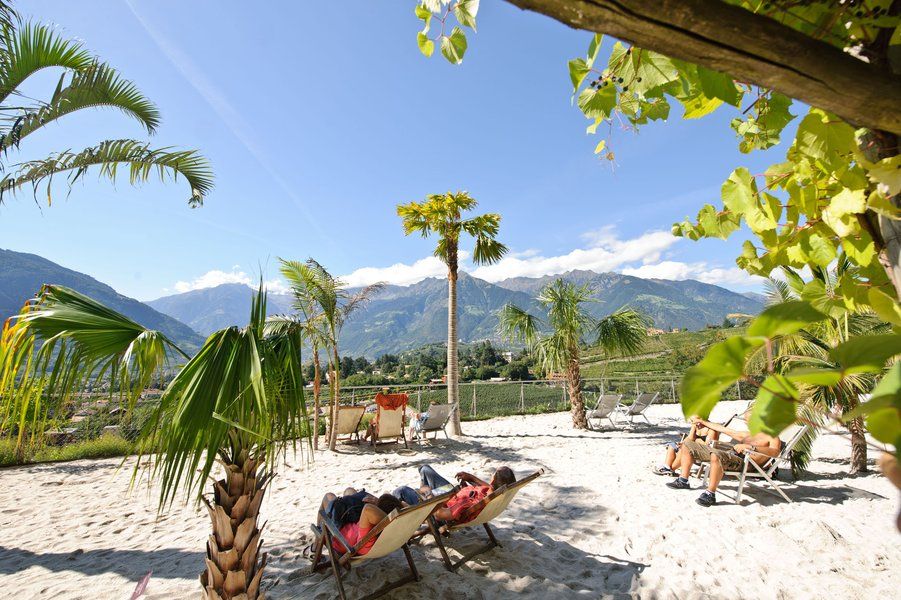 Sonniger Strand mit Liegestühlen, Palmen und Bergen im Hintergrund – ein entspannender Ort zum Relaxen.