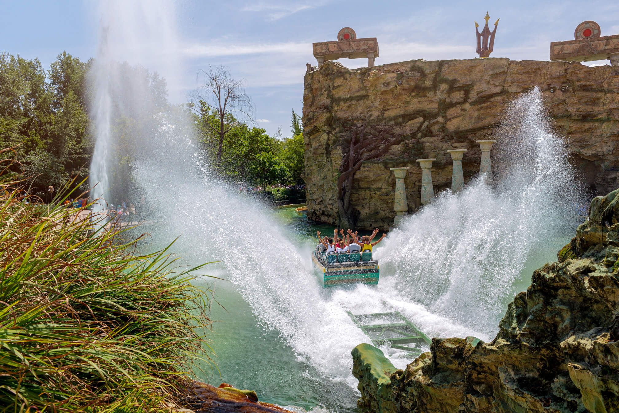Wasserfahrt in einem Freizeitpark mit jubelnden Passagieren und spritzendem Wasser vor einer beeindruckenden Kulisse.