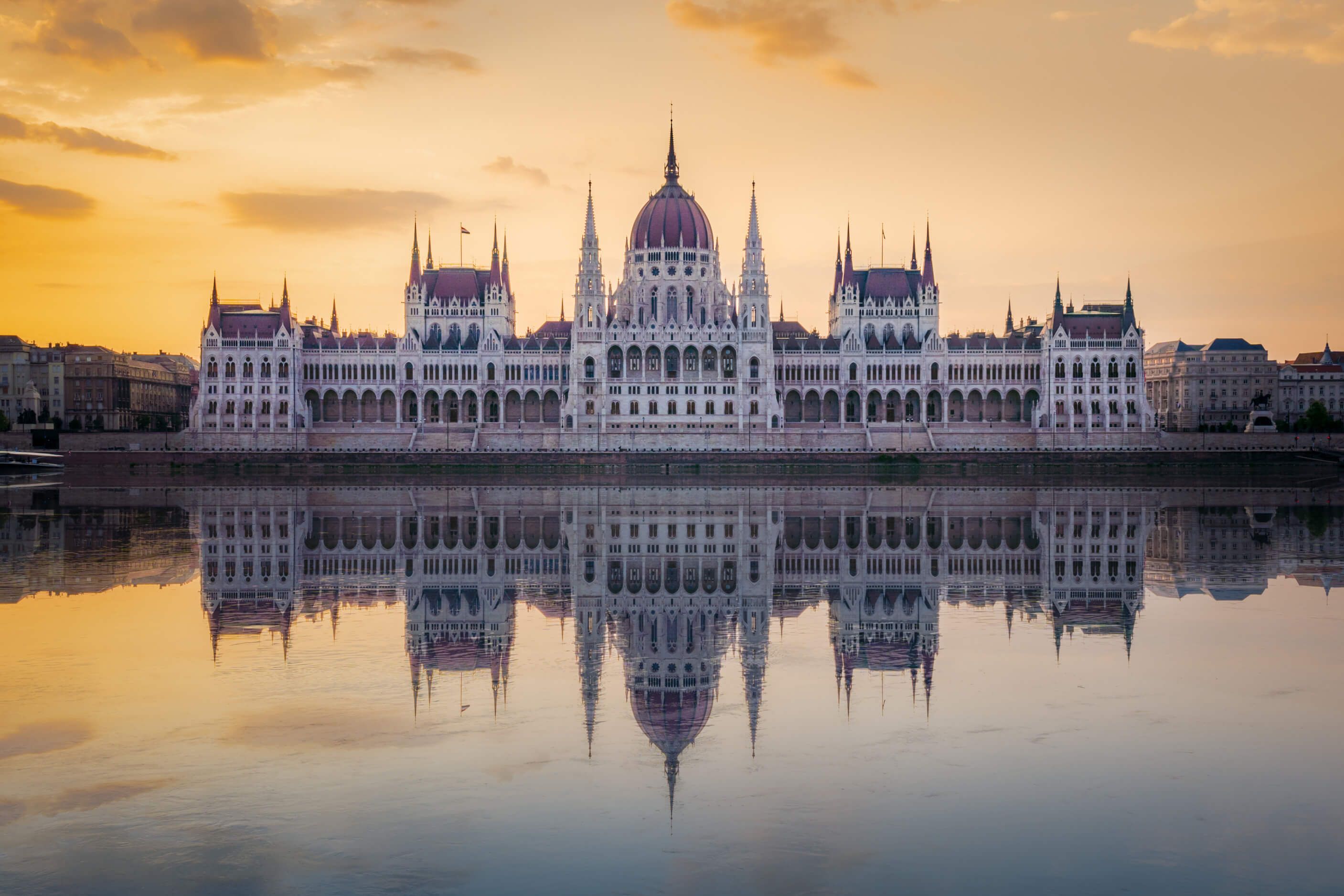 Das ungarische Parlamentsgebäude spiegelt sich im ruhigen Wasser bei Sonnenaufgang. Wunderschöne Architektur!