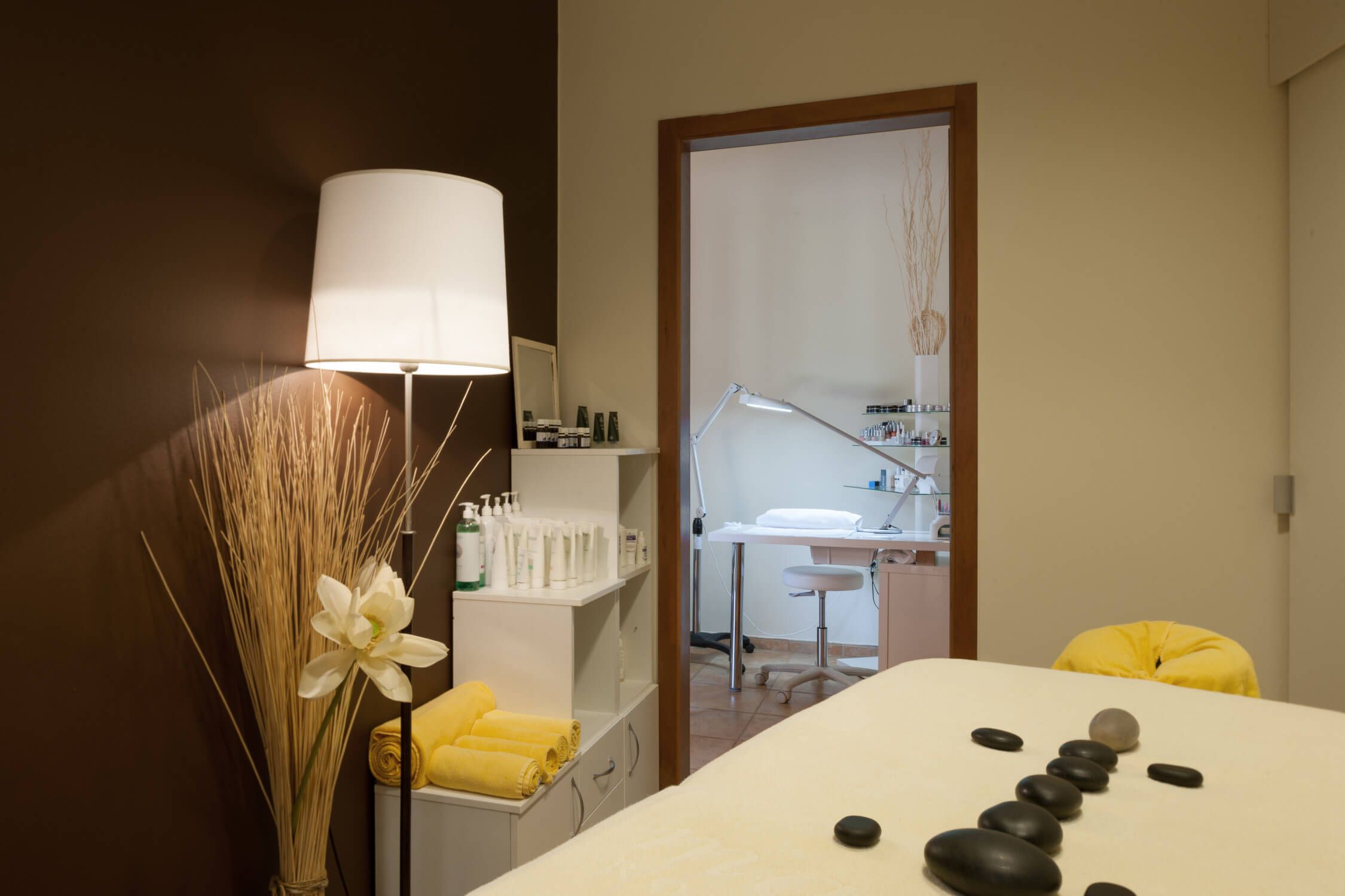 Ein ruhiger Wellnessbereich mit einer Massageliege, dekorativen Steinen und einem kosmetischen Arbeitsplatz im Hintergrund.