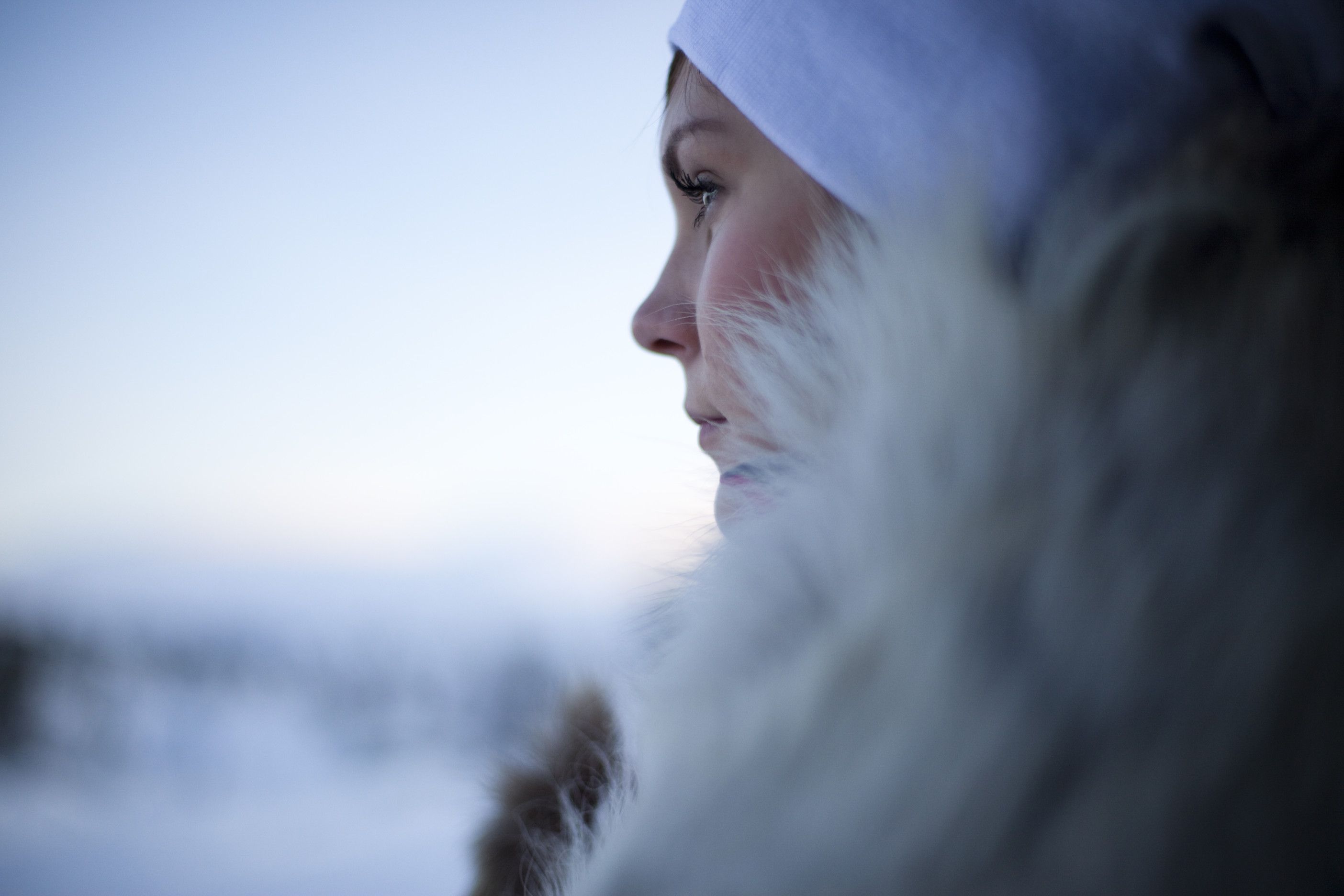 Eine Person in warmem Pelzmantel schaut nachdenklich in die kalte, schneebedeckte Umgebung.