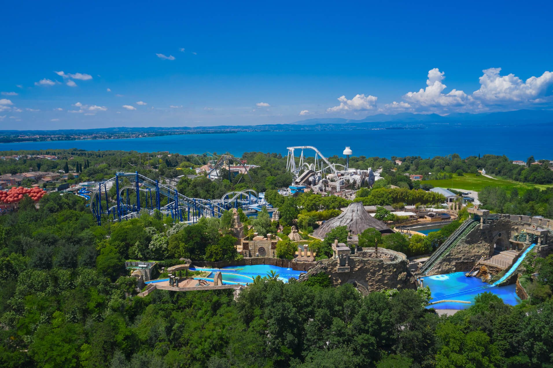 Ein Freizeitpark mit Achterbahnen, Wasserattraktionen und Blick auf einen schönen See unter blauem Himmel.