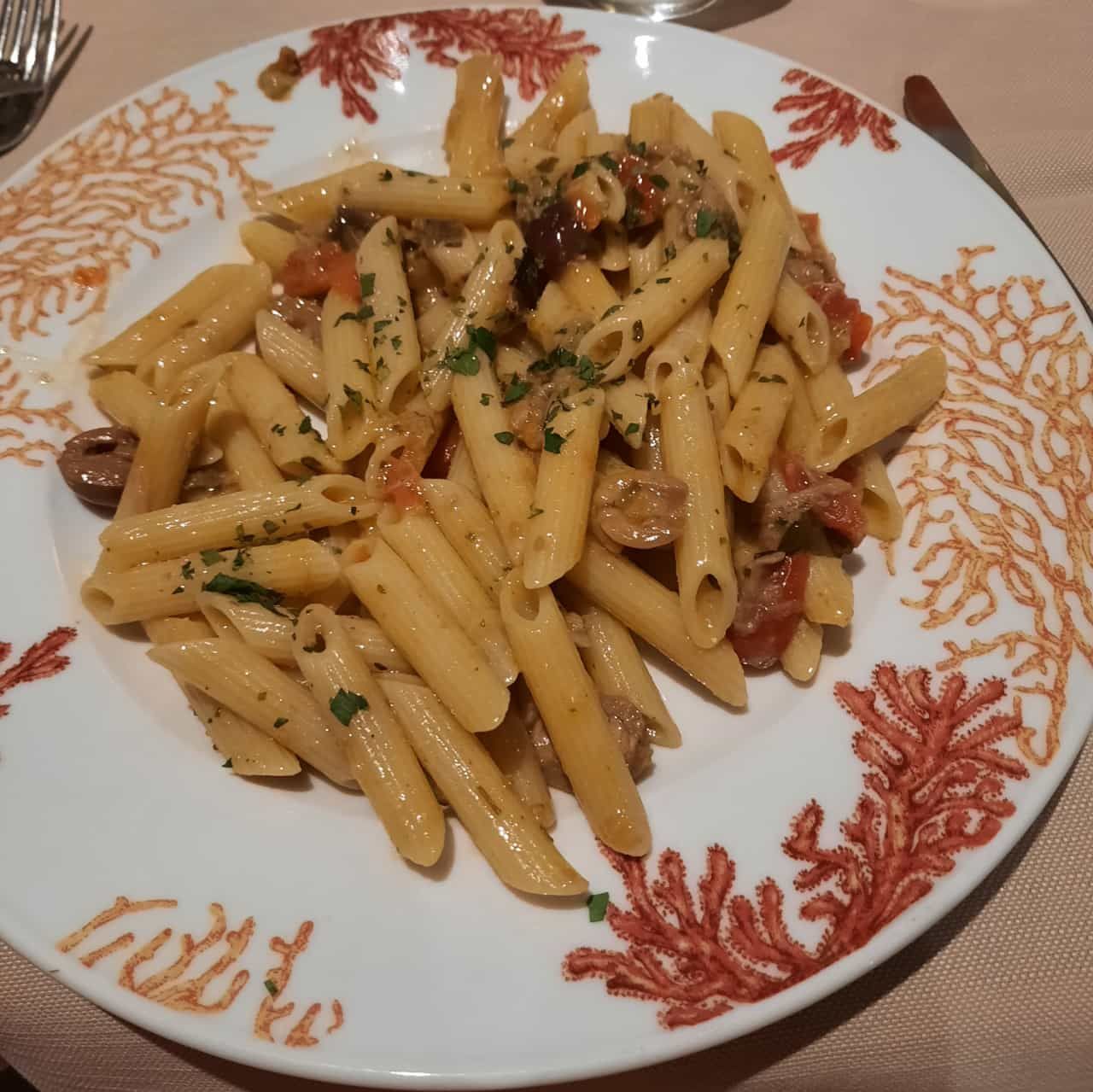 Penne-Pasta in einer cremigen Soße mit Tomaten und Kräutern auf einem dekorativen Teller serviert.