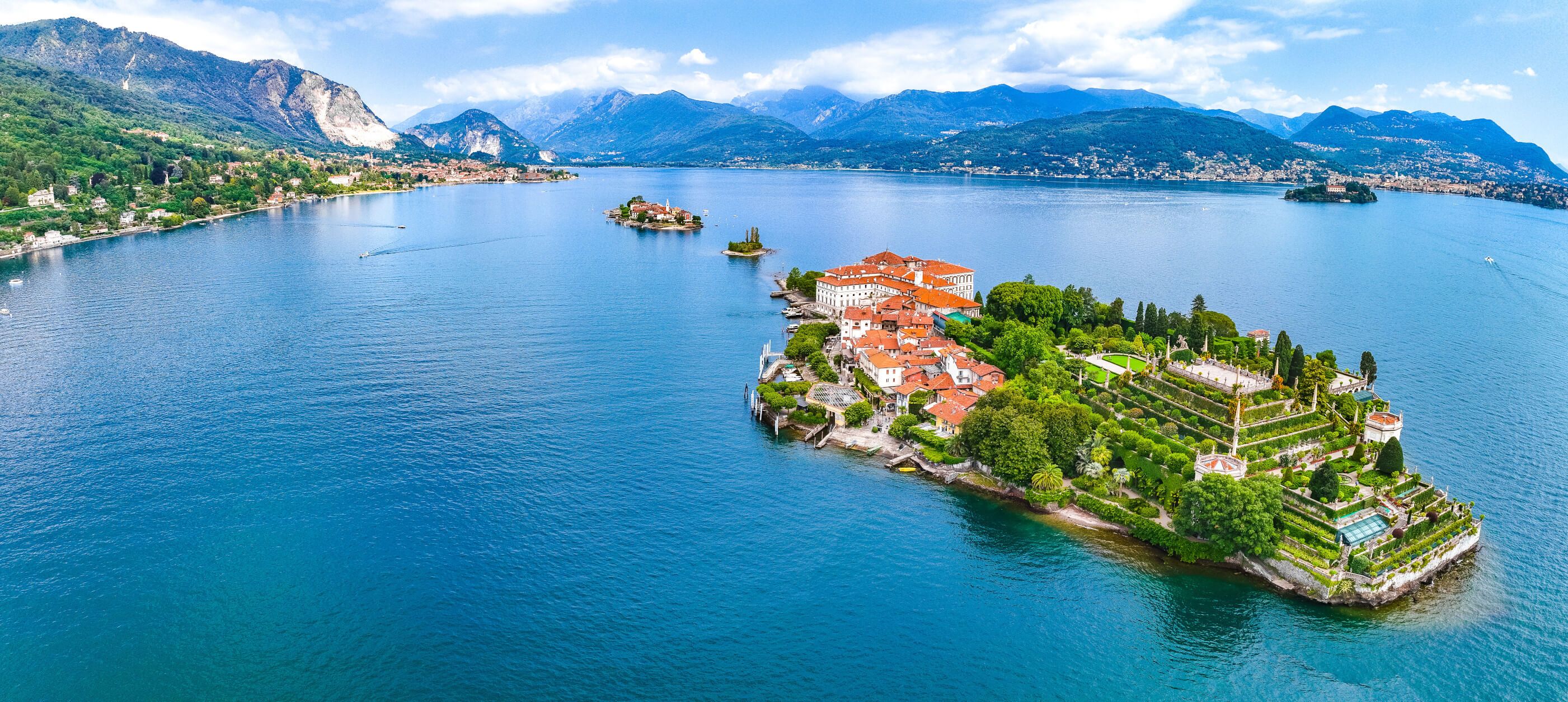 Eine malerische Seelandschaft mit einer Insel, üppigem Grün und historischen Gebäuden unter blauen Himmel.
