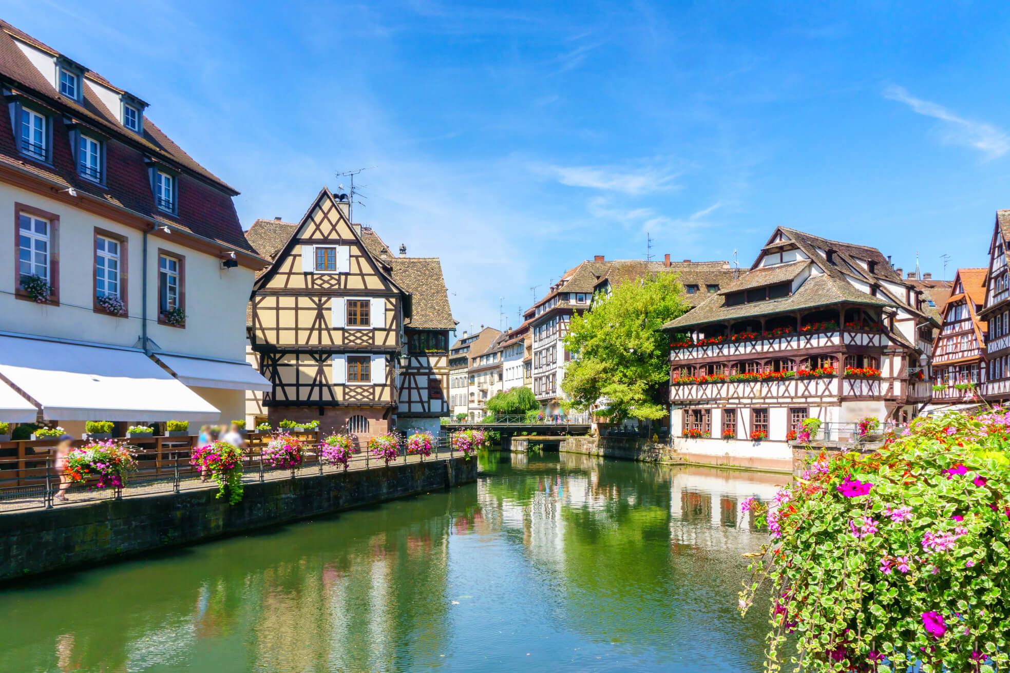 Friedliche Szene in Straßburg mit traditionellen Fachwerkhäusern und blühenden Blumen am Kanal unter blauem Himmel.