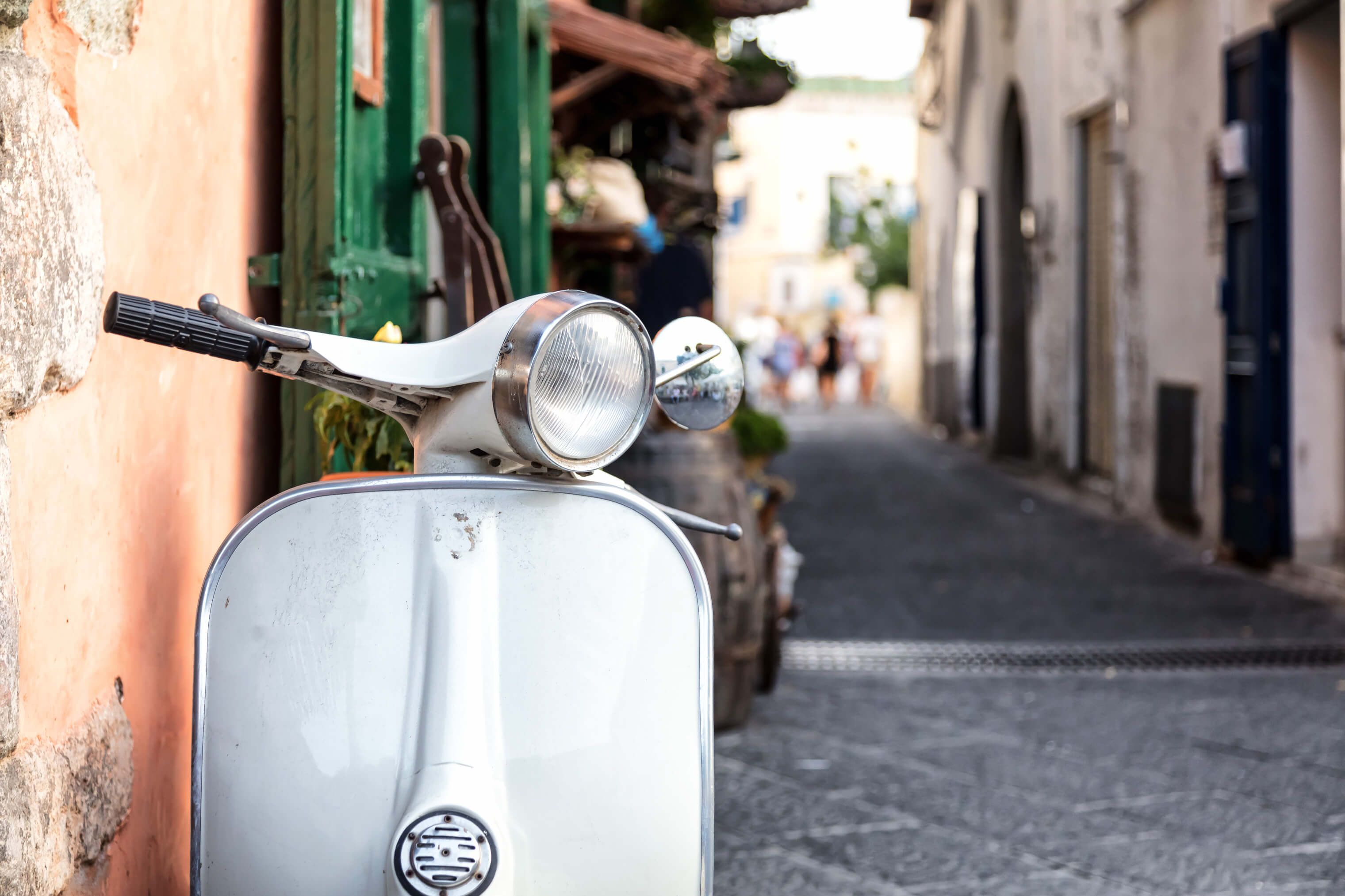 Ein alter, weißer Roller steht in einer malerischen Gasse zwischen bunten Gebäuden.
