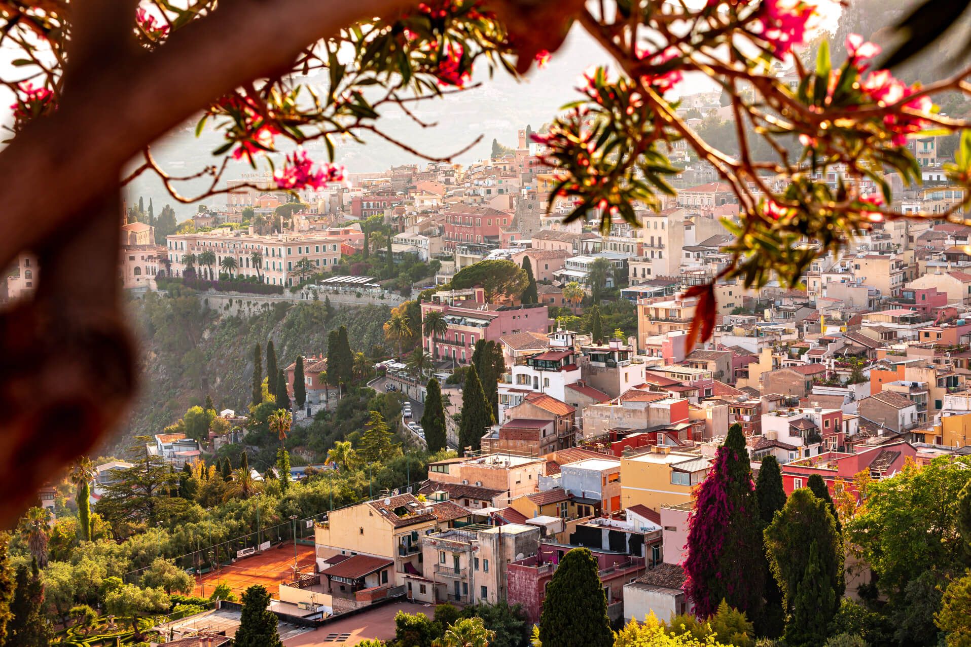 Blick auf eine malerische Stadt mit bunten Häusern, umgeben von Bäumen und bunten Blumen im Vordergrund.