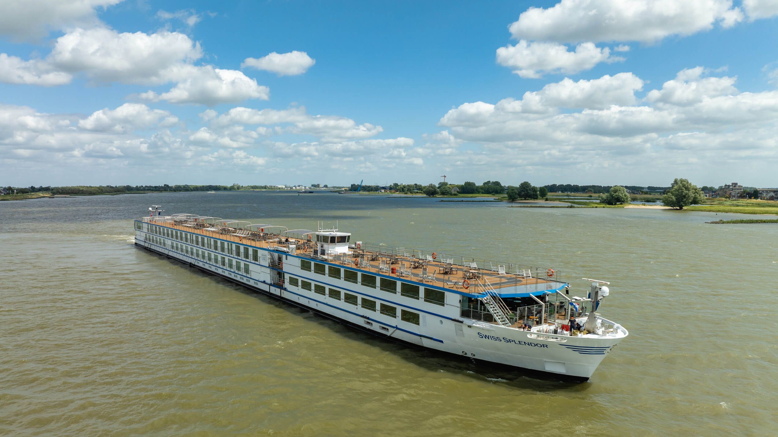 Ein Kreuzfahrtschiff gleitet über ruhiges Wasser, umgeben von Wolken und grüner Landschaft.