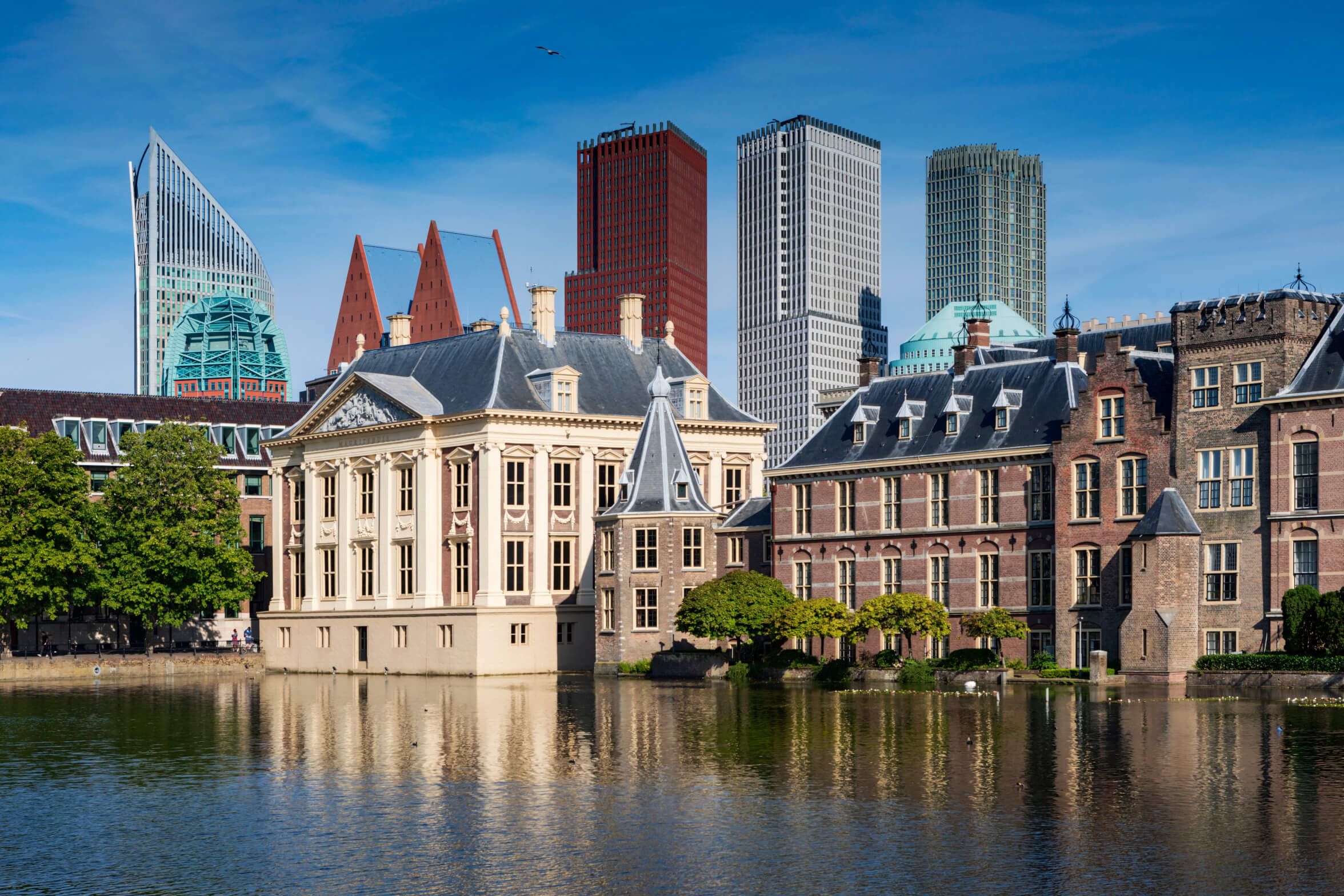 Das Bild zeigt historische Gebäude in Den Haag vor einer modernen Skylineszene und ruhigem Wasser.