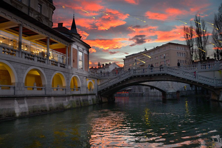 Eine malerische Abendansicht eines Flusses mit einer Brücke und bunten Wolken über der Stadt.